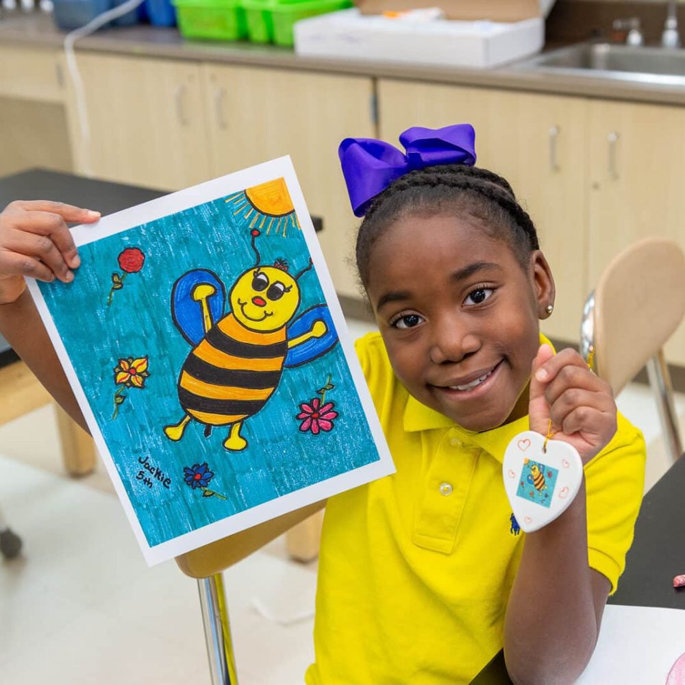 Host an Art Fundraiser for Schools by working with Art to Remember image shows girl holding up artwork